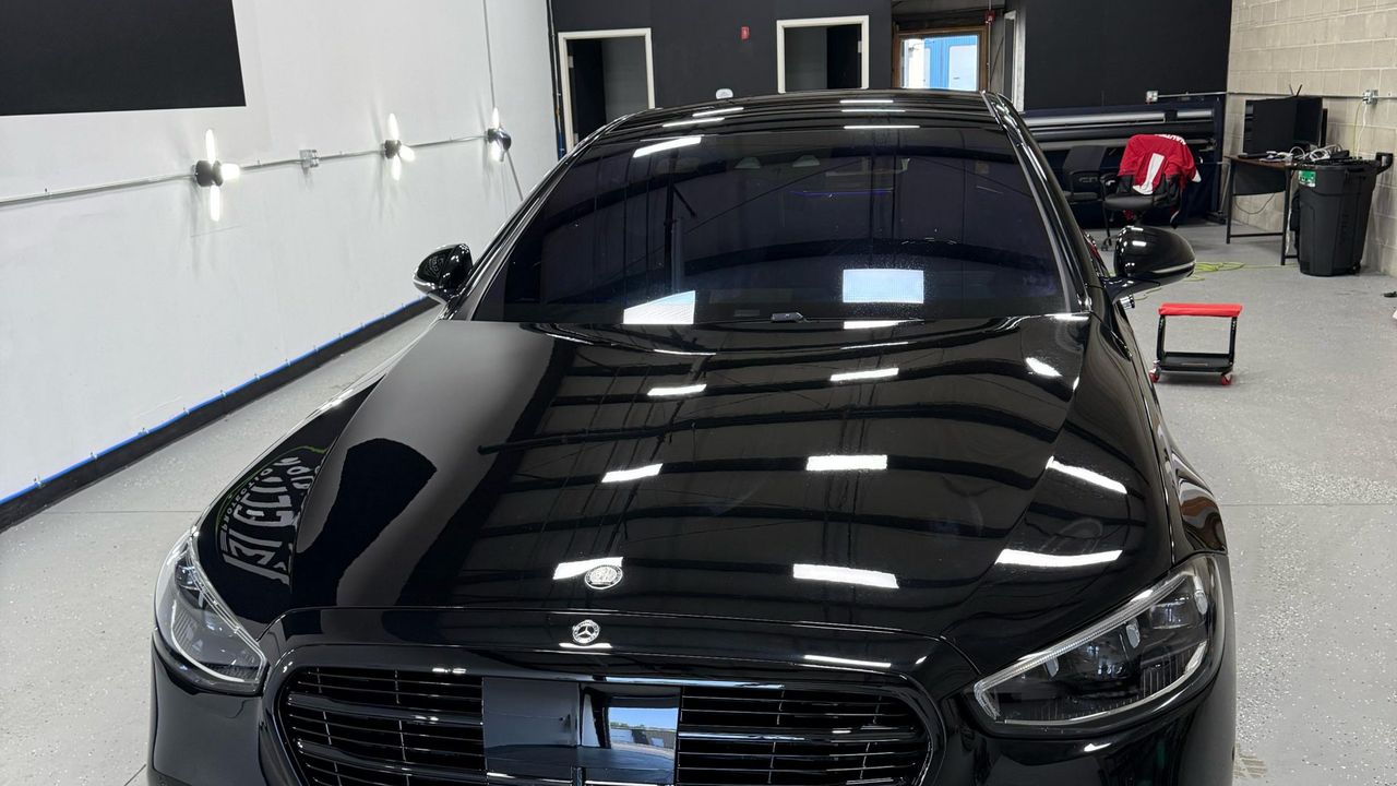 A black Mercedes-Benz S-Class with the shop ceiling lights reflected in unbroken lines across the hood.