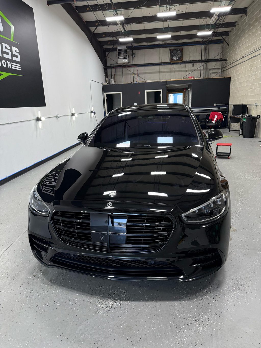 A black Mercedes-Benz S-Class with the ceiling lights reflected across the hood.