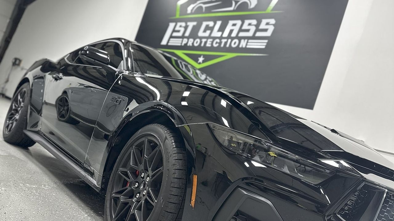 A black sports coupe in front of the 1st Class Protection wall sign.