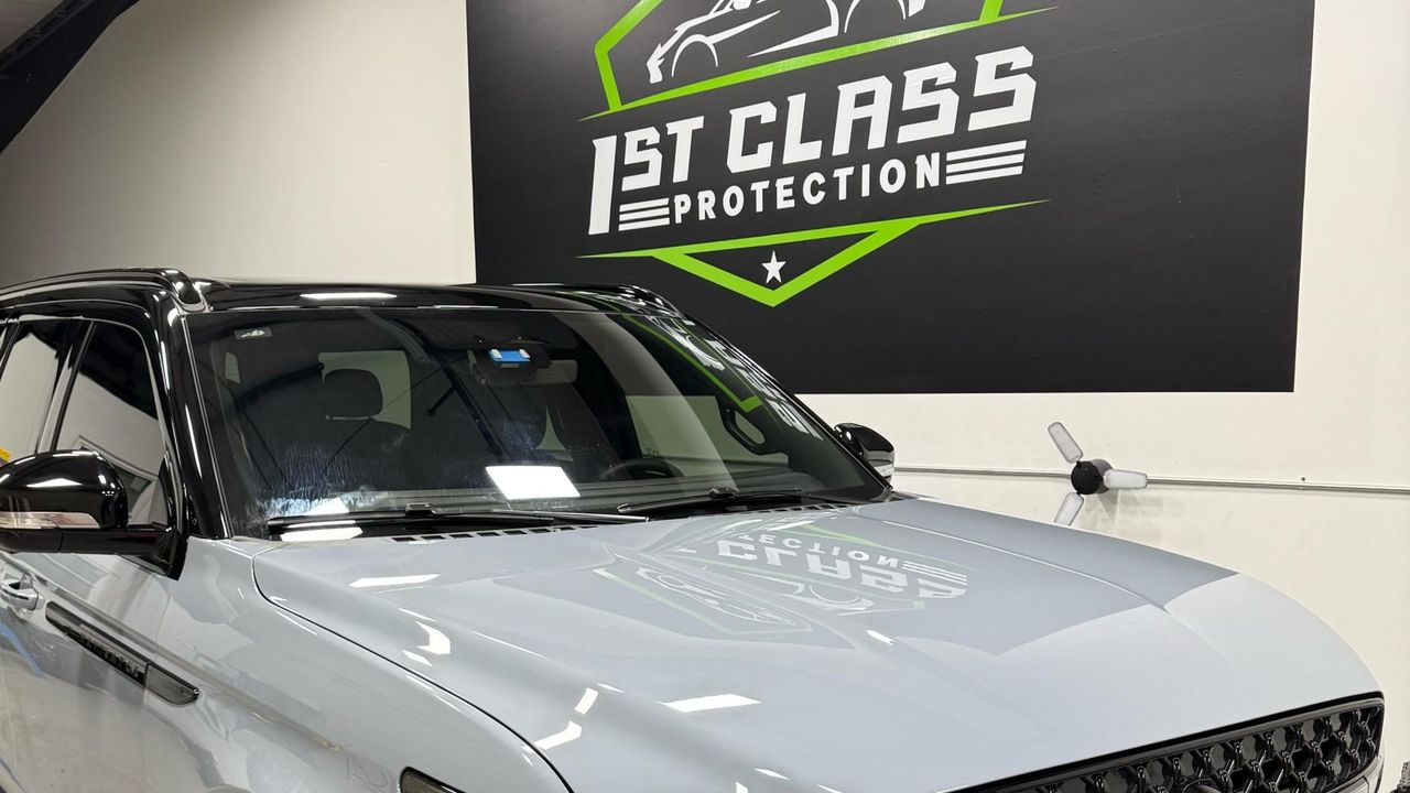 A white Lincoln Navigator in front of the 1st Class Protection wall sign.