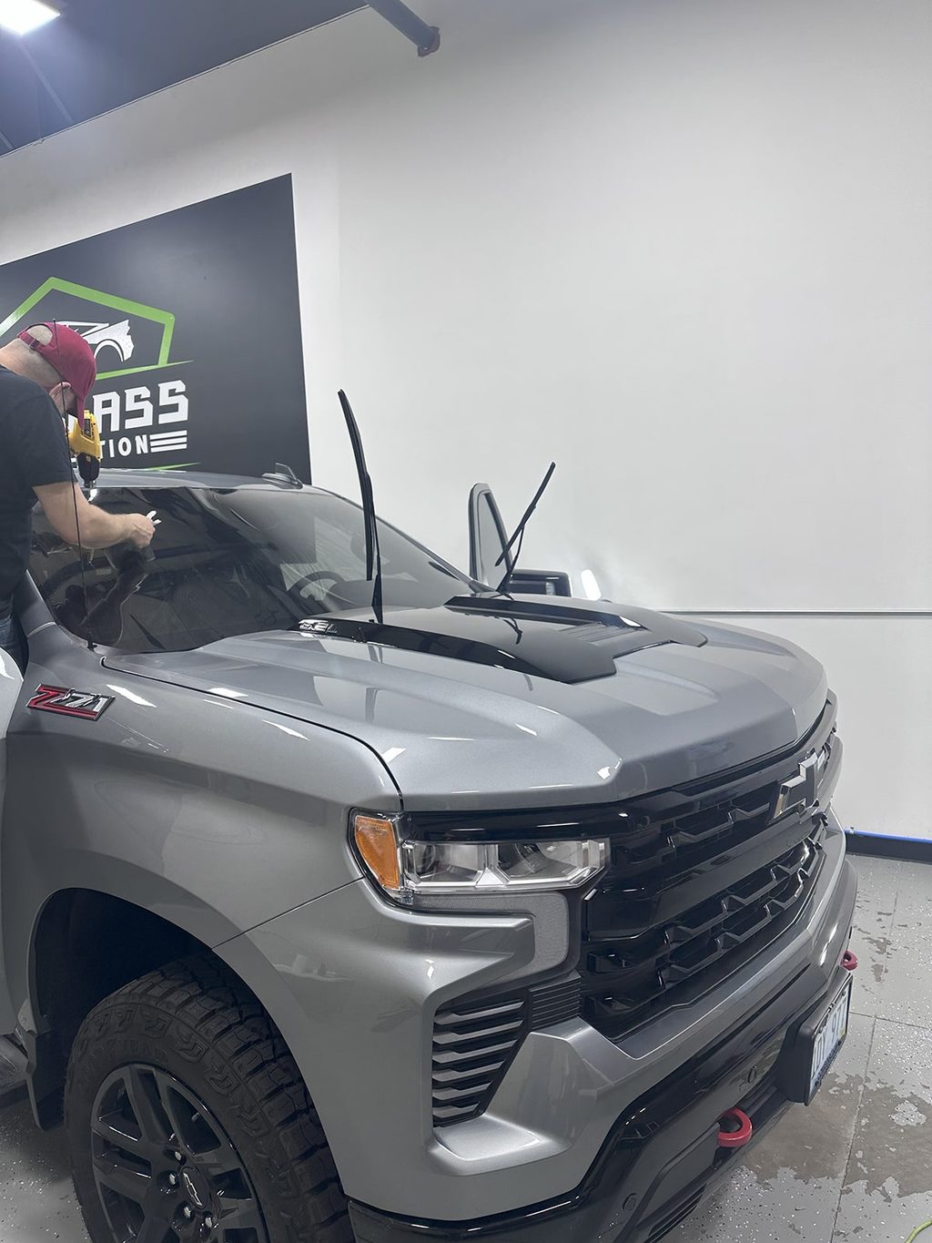 A technician working on the windshield area of a silver Chevrolet Silverado.