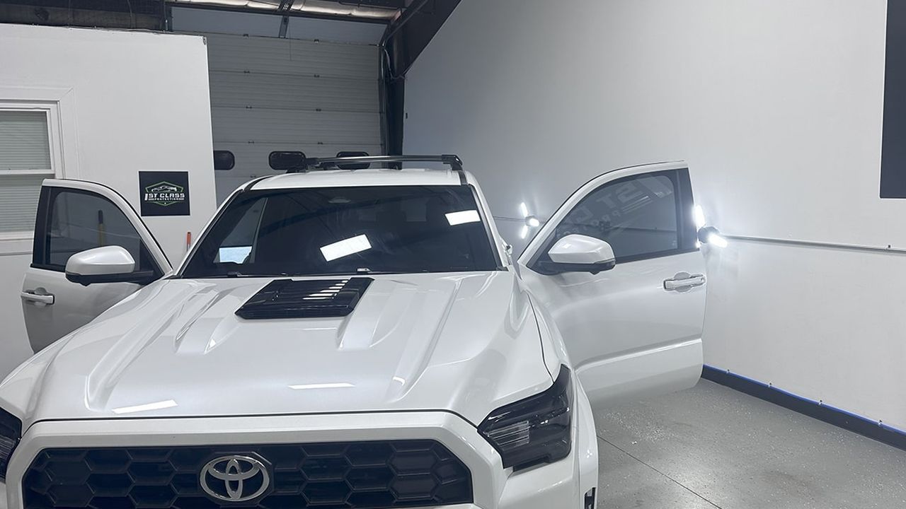 A white Toyota Tacoma with its doors open during installation in the 1st Class Protection shop.